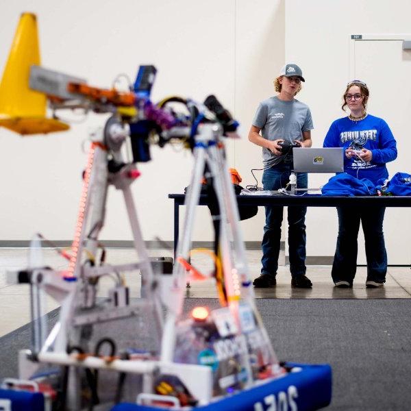 两个人站在一张桌子旁，前景是FIRST机器人公司的一个机器人